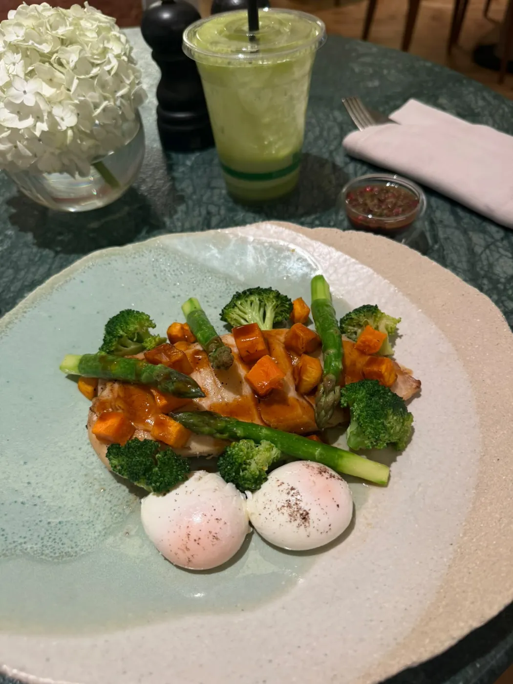 A plate of grilled chicken breast with sweet potato, asparagus, broccoli and two poached eggs, with a green juice.