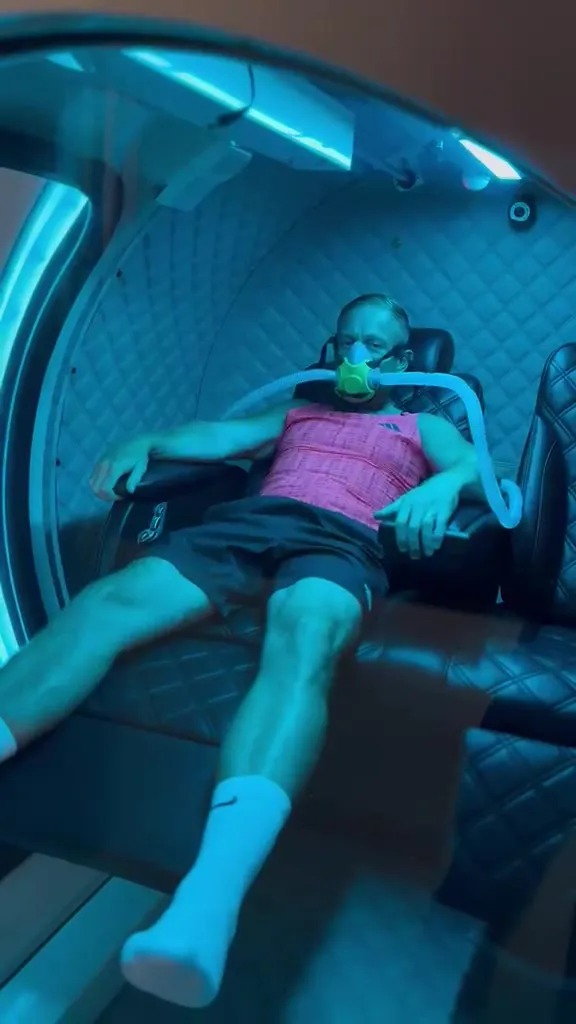 Bobby reclining inside a hyperbaric chamber wearing an oxygen mask.