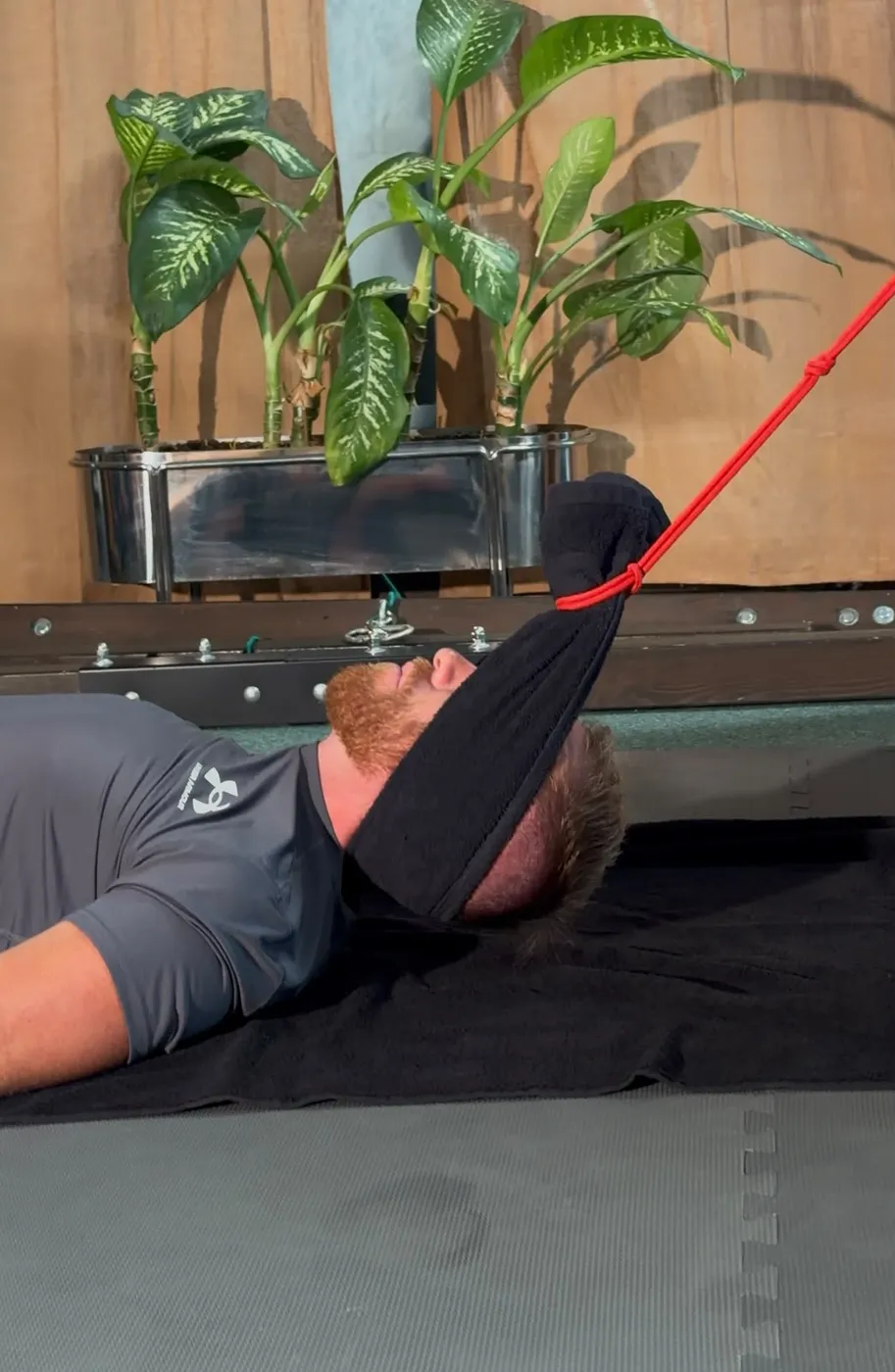 Bobby lying on a mat with a padded strap cradling his head for an assisted neck stretch.
